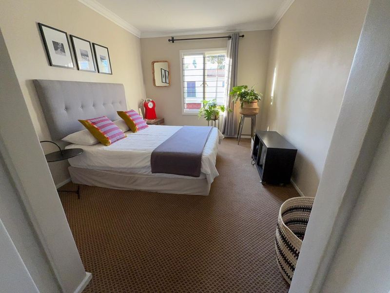 A well-lit bedroom featuring carpeted flooring, a window with security bars, and neutral wall finishes.