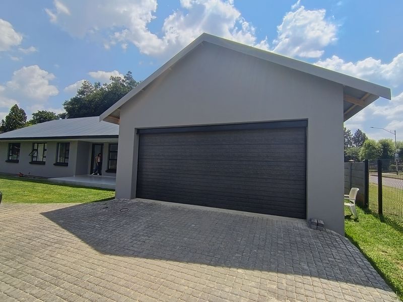Front view of the property featuring a paved driveway, a modern garage door, and a covered entrance patio.