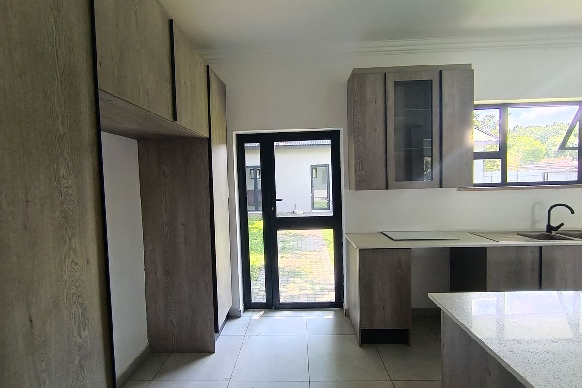 Modern kitchen featuring wood-look cabinetry, stone countertops, tiled flooring, and direct access to the rear garden through a glass-panelled door.