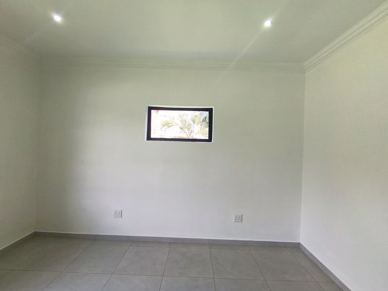 A clean, empty bedroom featuring neutral tiled flooring, recessed downlights, and a small horizontal window, providing a blank canvas for interior design.