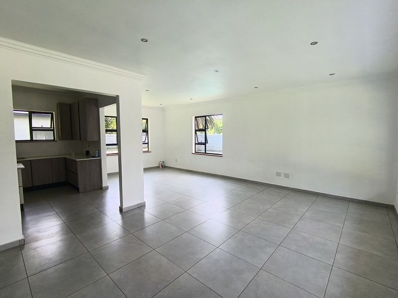 Spacious open-plan living area featuring neutral tiled flooring, recessed lighting, and an integrated kitchen space with modern cabinetry.