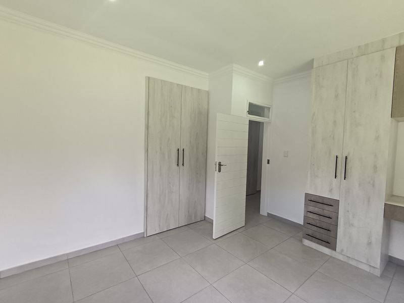 A bright, modern bedroom featuring neutral tiled flooring, built-in cupboards with a contemporary wood-grain finish, and clean white walls.