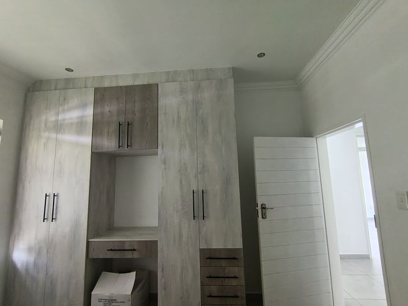 A bedroom featuring modern built-in cupboards with a central vanity area, recessed lighting, and neutral tiled flooring.