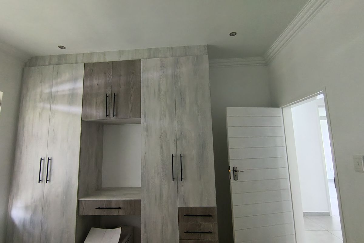 A bedroom featuring modern built-in cupboards with a central vanity area, recessed lighting, and neutral tiled flooring.
