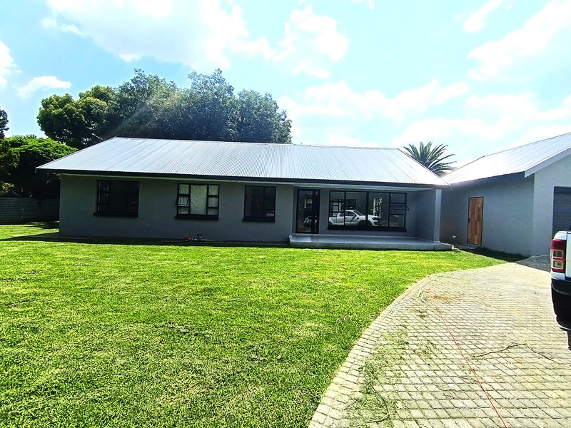 Front view of a well-maintained single-story house featuring a corrugated metal roof, paved driveway, and a spacious front lawn.