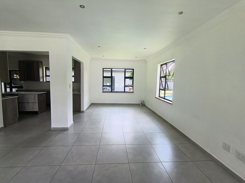 Spacious open-plan living area featuring neutral tiled flooring, recessed lighting, and a seamless transition to a modern kitchen with built-in cabinetry.