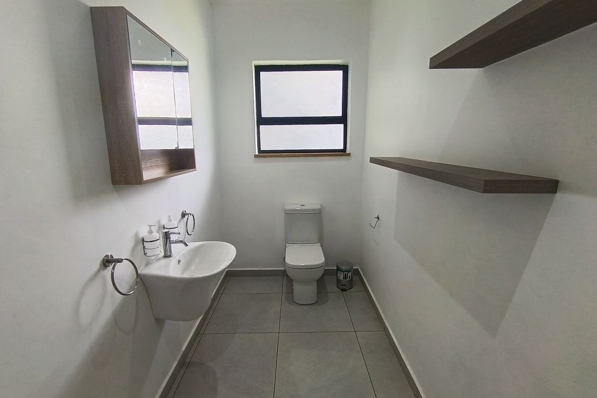 A clean and modern bathroom featuring a wall-mounted basin, toilet, medicine cabinet, and floating shelving with neutral floor tiles.