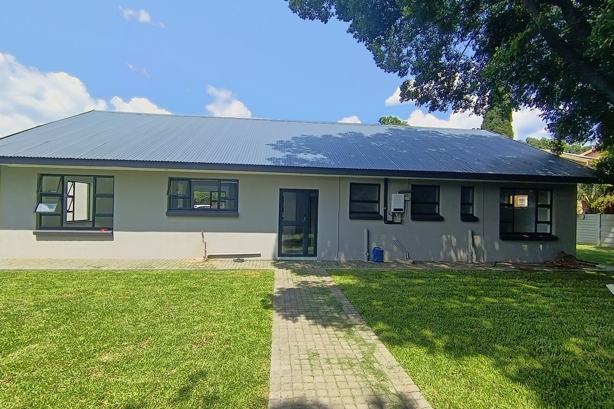 Rear view of the house featuring a corrugated metal roof, paved walkway, and well-maintained lawn with modern aluminium window and door frames.