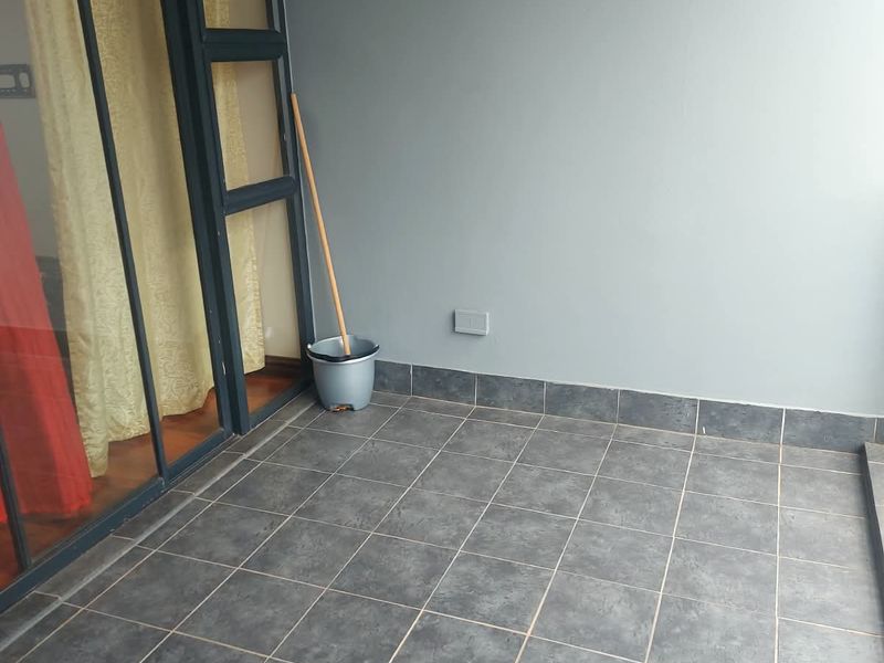 A clean, tiled balcony area featuring a sliding glass door entrance and a wall-mounted light fixture, providing a functional outdoor space.