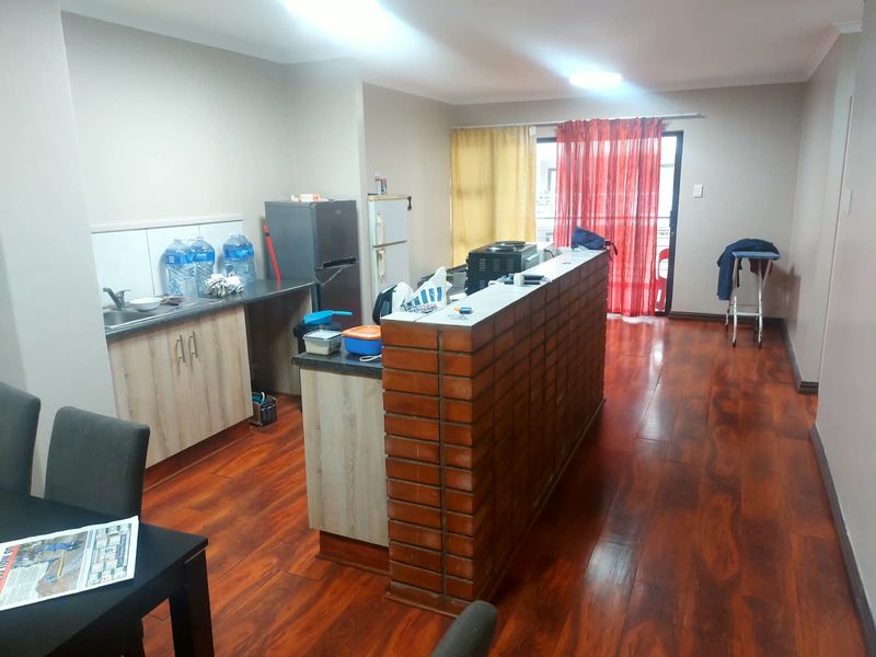 Open plan living area featuring laminate flooring, a brick breakfast bar, and a functional kitchen space with direct access to a balcony.