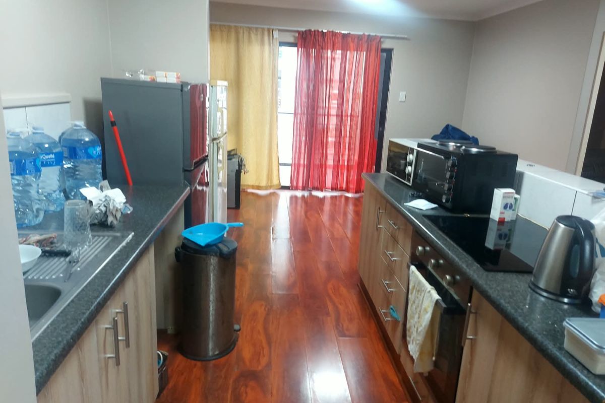 A functional kitchen featuring laminate cabinetry, dark countertops, built-in oven and hob, with warm-toned laminate flooring and access to a balcony.