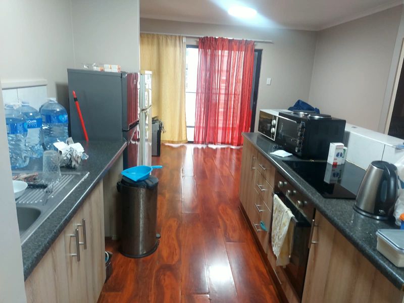A functional kitchen featuring laminate cabinetry, dark countertops, built-in oven and hob, with warm-toned laminate flooring and access to a balcony.