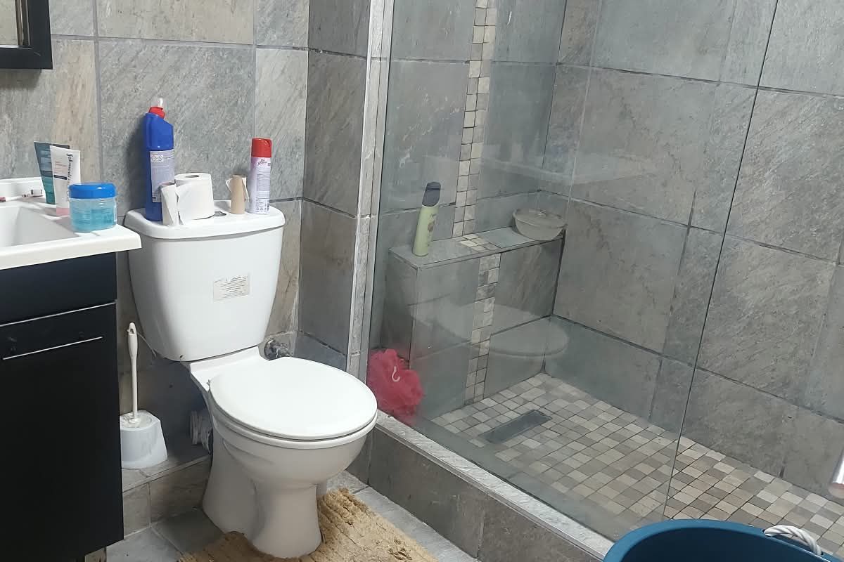 A functional bathroom featuring a walk-in shower with glass enclosure, vanity cabinet, and grey tiled finishes throughout.