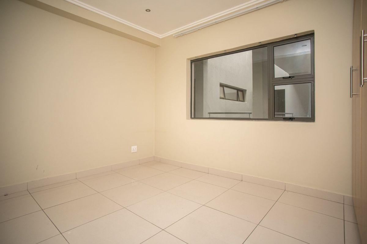 A clean, empty bedroom featuring neutral tiled flooring, built-in cupboards, and modern aluminium window frames, providing a versatile space ready for personalization.