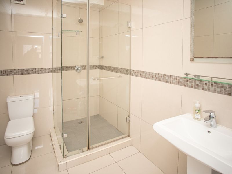 A clean and modern bathroom featuring a glass-enclosed shower, pedestal basin, and neutral wall and floor tiling.