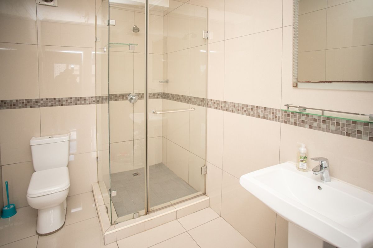 A clean and modern bathroom featuring a glass-enclosed shower, pedestal basin, and neutral wall and floor tiling.