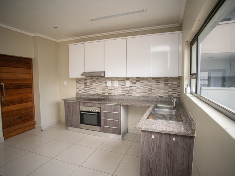 A clean, modern kitchen featuring white upper cabinets, wood-grain lower cabinetry, granite countertops, and integrated appliances, finished with neutral floor tiles.