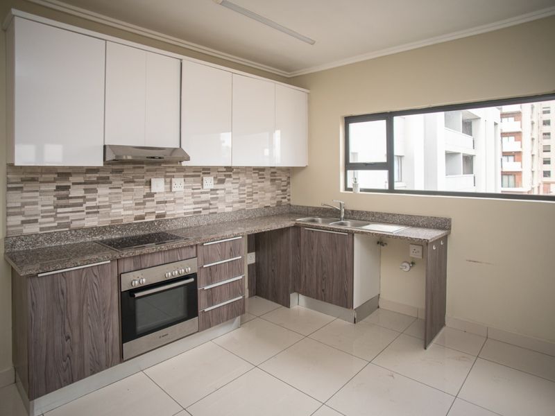 A modern, empty kitchen featuring white and wood-grain cabinetry, granite countertops, a mosaic backsplash, and integrated appliances including an oven and hob.