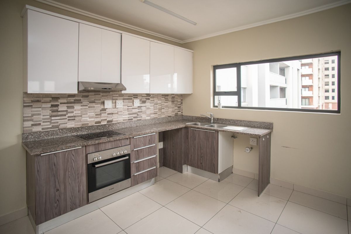 A modern, empty kitchen featuring white and wood-grain cabinetry, granite countertops, a mosaic backsplash, and integrated appliances including an oven and hob.