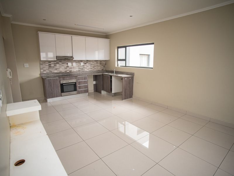 An open-plan kitchen area featuring modern cabinetry, granite countertops, a mosaic backsplash, and tiled flooring, presented in a clean, vacant state.