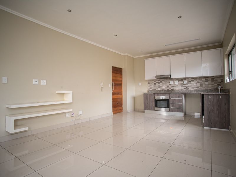 Spacious open-plan living area featuring a modern kitchen with built-in cabinetry, granite countertops, integrated oven, and sleek tiled flooring throughout.