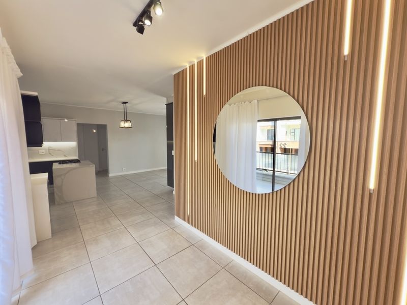 Modern open-plan living area featuring stylish slatted timber wall paneling with integrated LED lighting, tiled floors, and a contemporary kitchen with stone island.