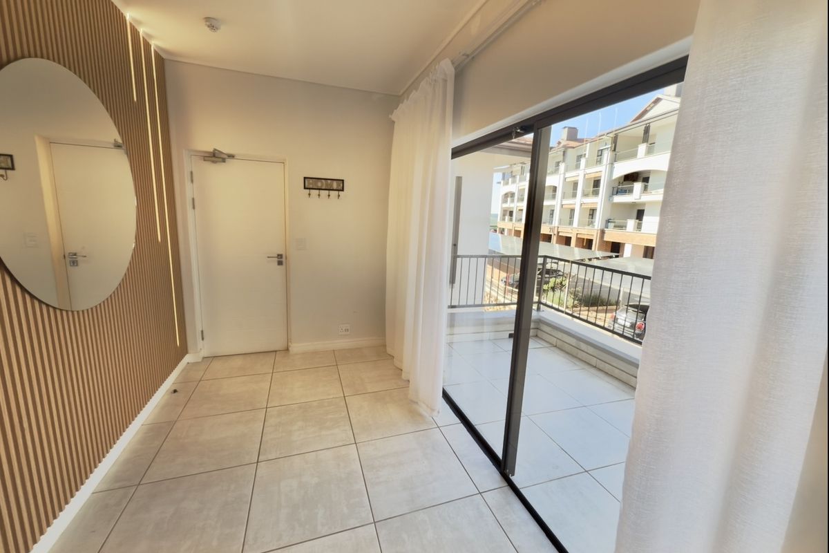 Bright living area featuring modern slatted wood wall paneling, large format floor tiles, and a sliding glass door leading to a private balcony.