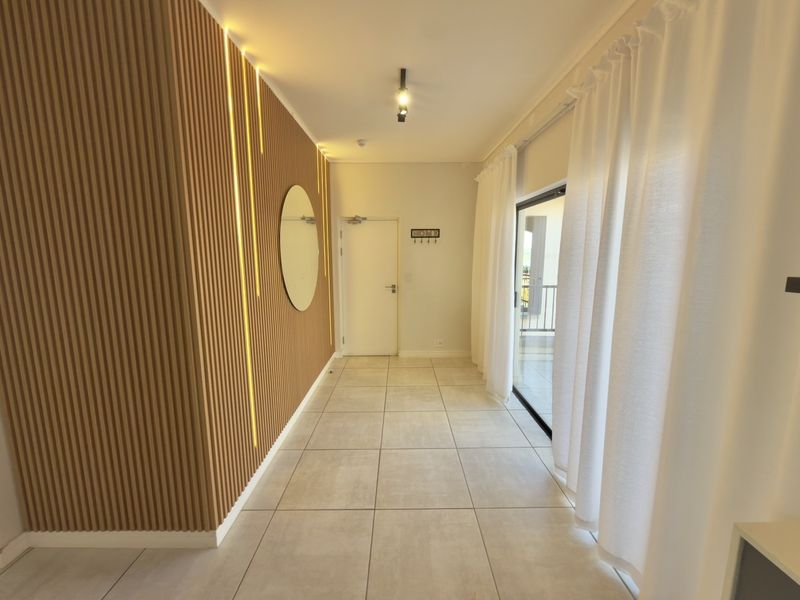 A modern, well-lit hallway featuring contemporary slatted timber wall paneling with integrated LED lighting and large format floor tiles leading to a balcony.