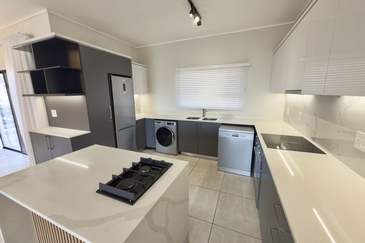Modern kitchen featuring sleek cabinetry, quartz countertops, a central island with a gas hob, and integrated appliances in a well-lit, contemporary space.