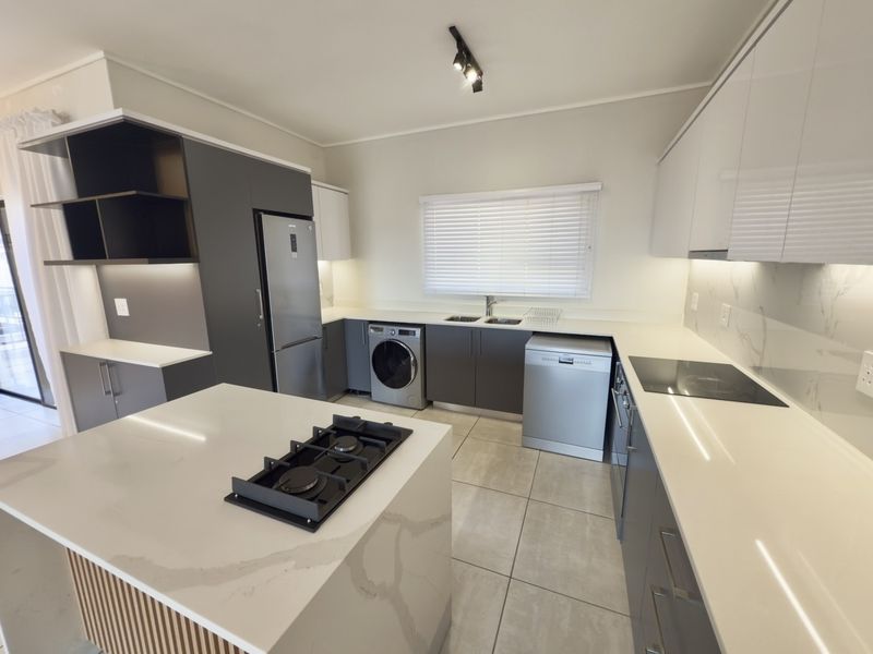 Modern kitchen featuring sleek cabinetry, quartz countertops, a central island with a gas hob, and integrated appliances in a well-lit, contemporary space.