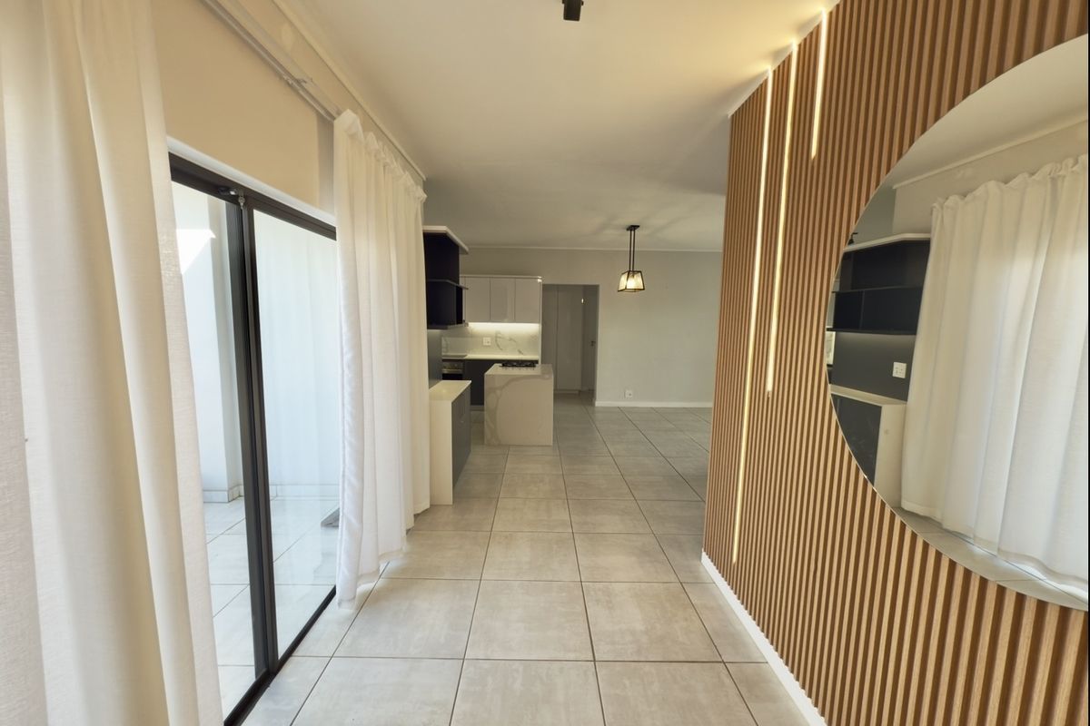 Modern open-plan living area featuring a striking slatted timber feature wall with integrated lighting, large format floor tiles, and seamless access to the balcony.