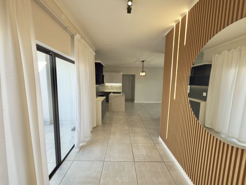 Modern open-plan living area featuring a striking slatted timber feature wall with integrated lighting, large format floor tiles, and seamless access to the balcony.