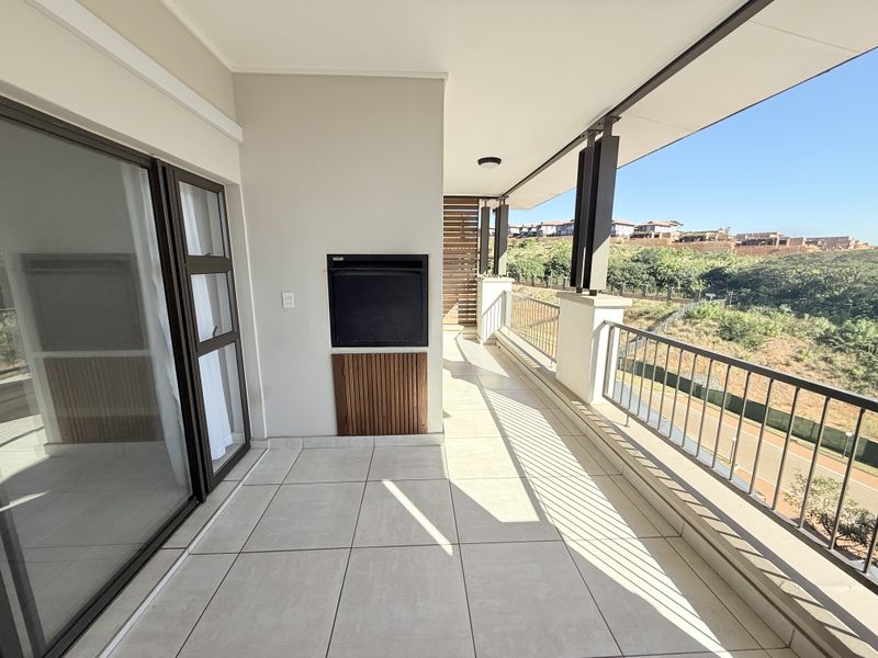 Spacious covered balcony featuring tiled flooring, a built-in braai, and metal balustrades, offering scenic views of the surrounding landscape.