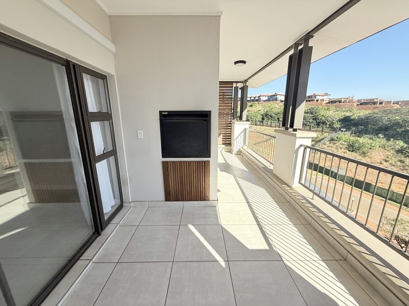 A spacious covered balcony featuring tiled flooring, a built-in braai, and metal balustrades, offering an open outdoor area perfect for entertaining.