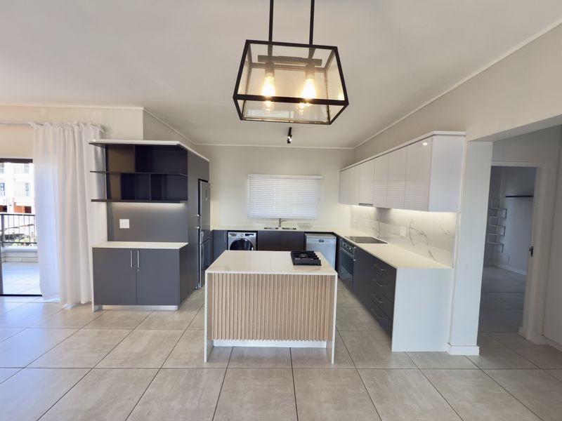 Modern open-plan kitchen featuring a central island, sleek cabinetry, stone countertops, integrated appliances, and contemporary pendant lighting in a bright, tiled space.