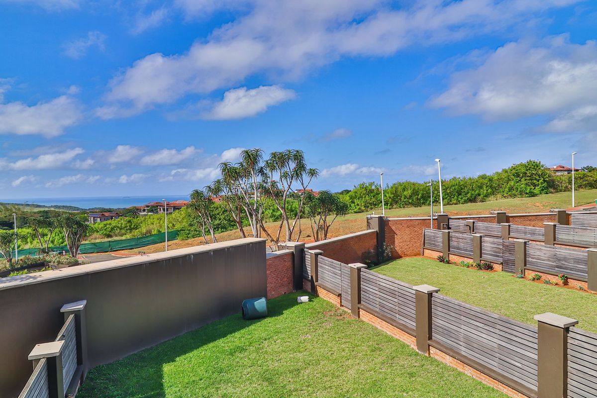 A well-maintained rear garden area featuring brick boundary walls, timber slat fencing, and a manicured lawn with scenic coastal views.