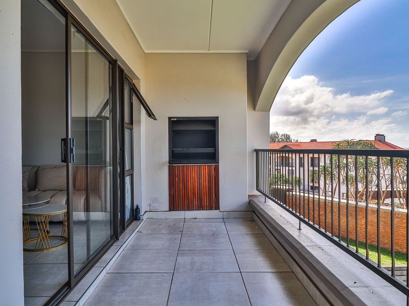 A spacious covered balcony featuring tiled flooring, a built-in braai, and a metal balustrade, offering a pleasant outdoor area for relaxation.