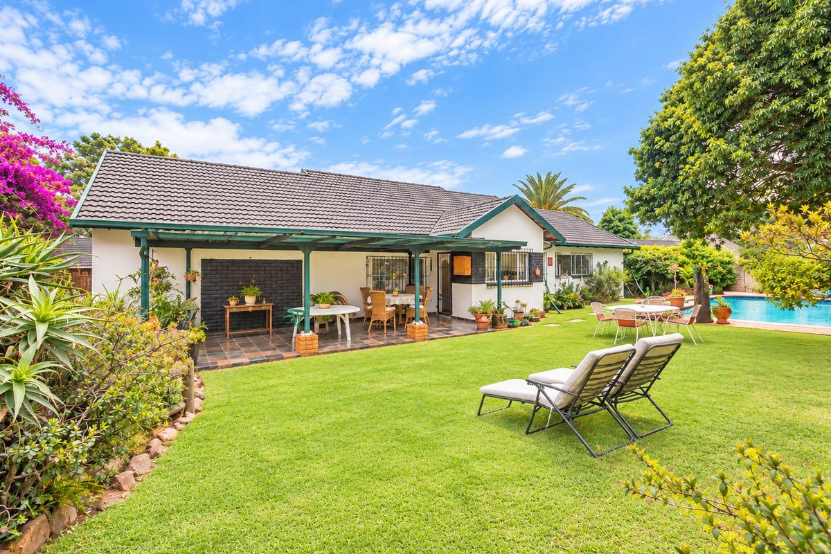 Rear view of the property featuring a covered patio, well-maintained lawn, and a swimming pool in a landscaped garden setting.