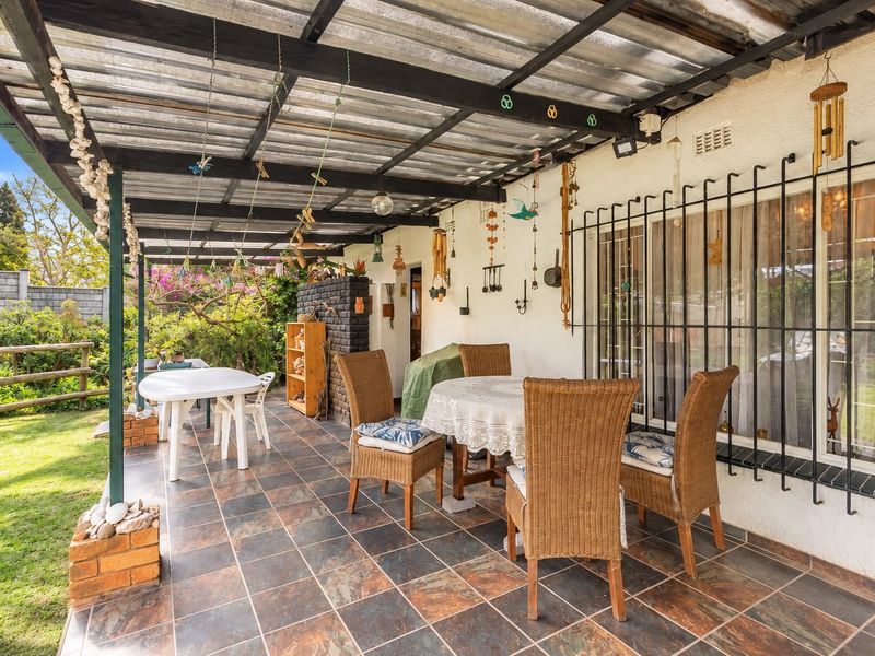 Covered outdoor patio area featuring tiled flooring, a corrugated metal roof structure, and security bars on the windows, overlooking the garden.