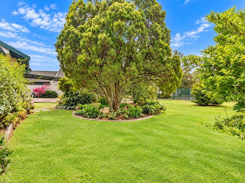 A well-maintained rear garden featuring a lush green lawn, mature trees, and established garden beds with brick edging.