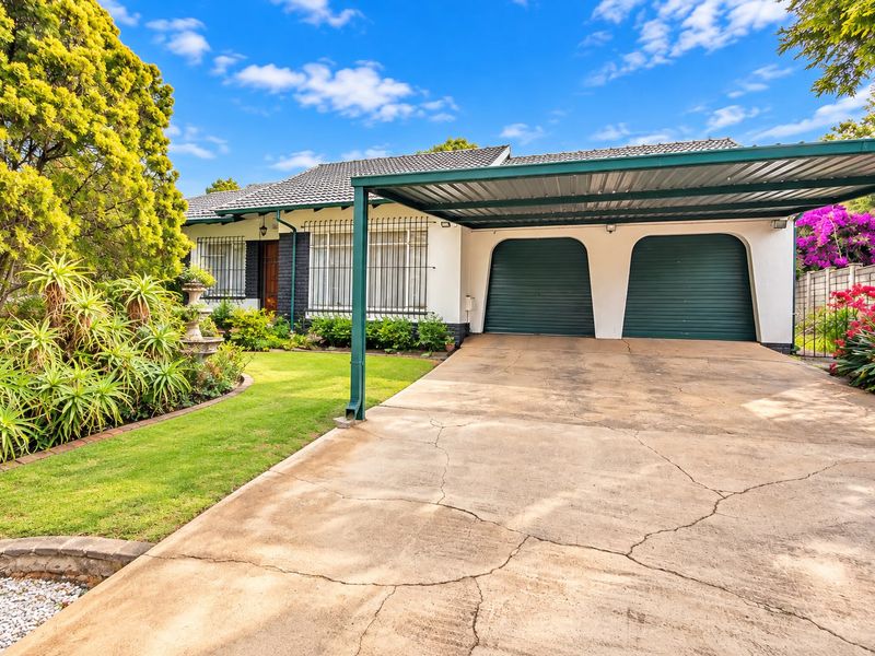 Front elevation of a house featuring a double garage, attached carport, and a landscaped garden with a concrete driveway.
