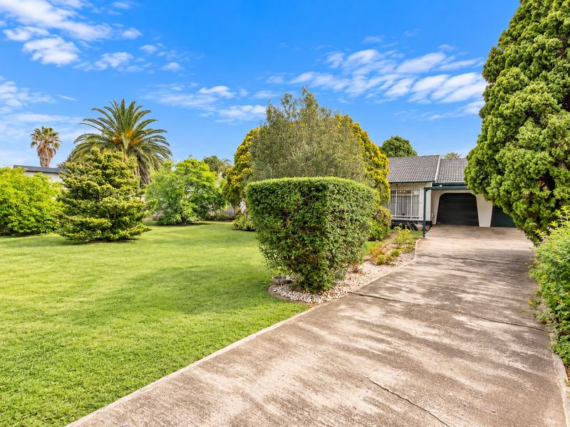 Front view of the property featuring a spacious lawn, mature garden landscaping, and a concrete driveway leading to the garage.