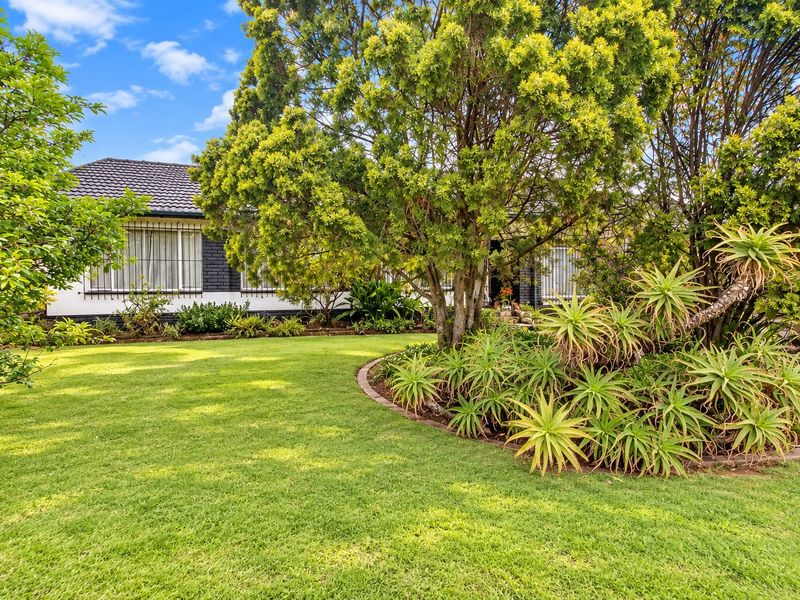 Front view of the house featuring a well-maintained lawn, mature garden beds with brick edging, and a tiled roof structure.