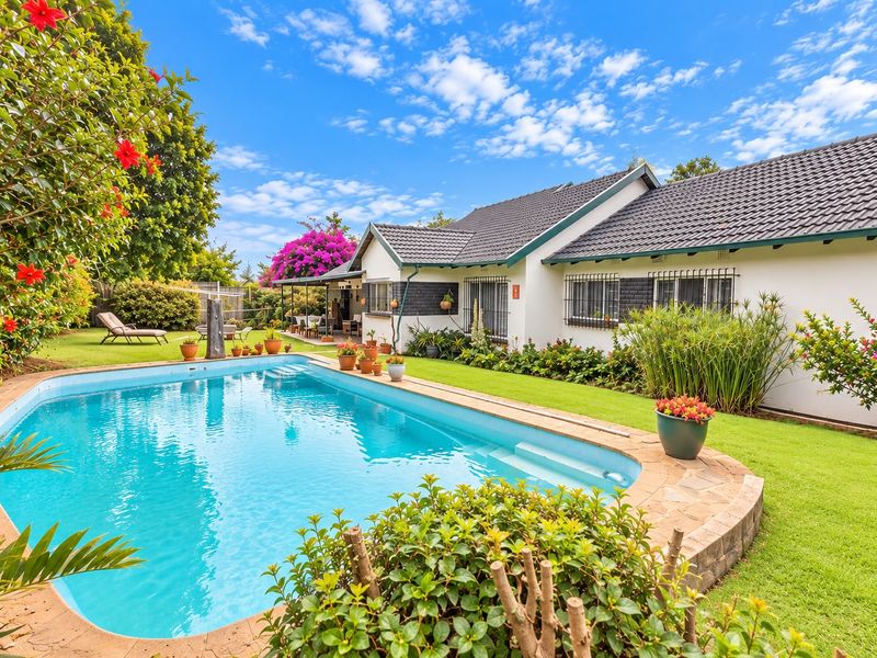 A well-maintained rear garden featuring a swimming pool with tiled coping, lush lawn, and a covered patio area attached to the main house.