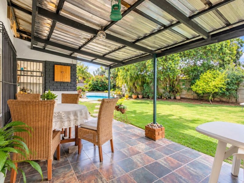 Covered outdoor patio featuring tiled flooring and a corrugated roof, overlooking a private garden and swimming pool area.