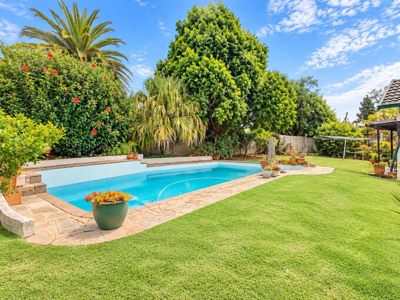 A well-maintained backyard featuring a swimming pool with stone coping, surrounded by a lush lawn and mature garden landscaping.