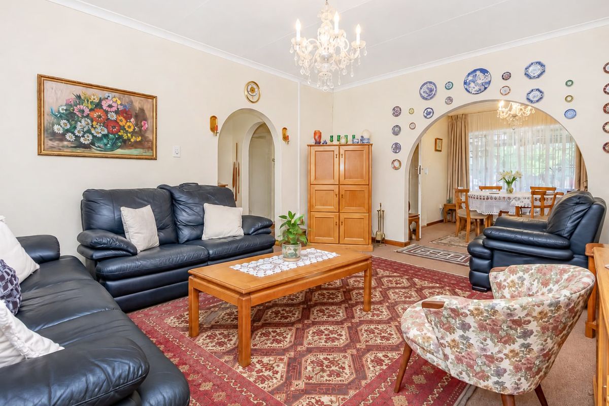 A spacious living room featuring classic archways, decorative coving, and a central chandelier, providing a traditional layout with access to the adjoining dining area.