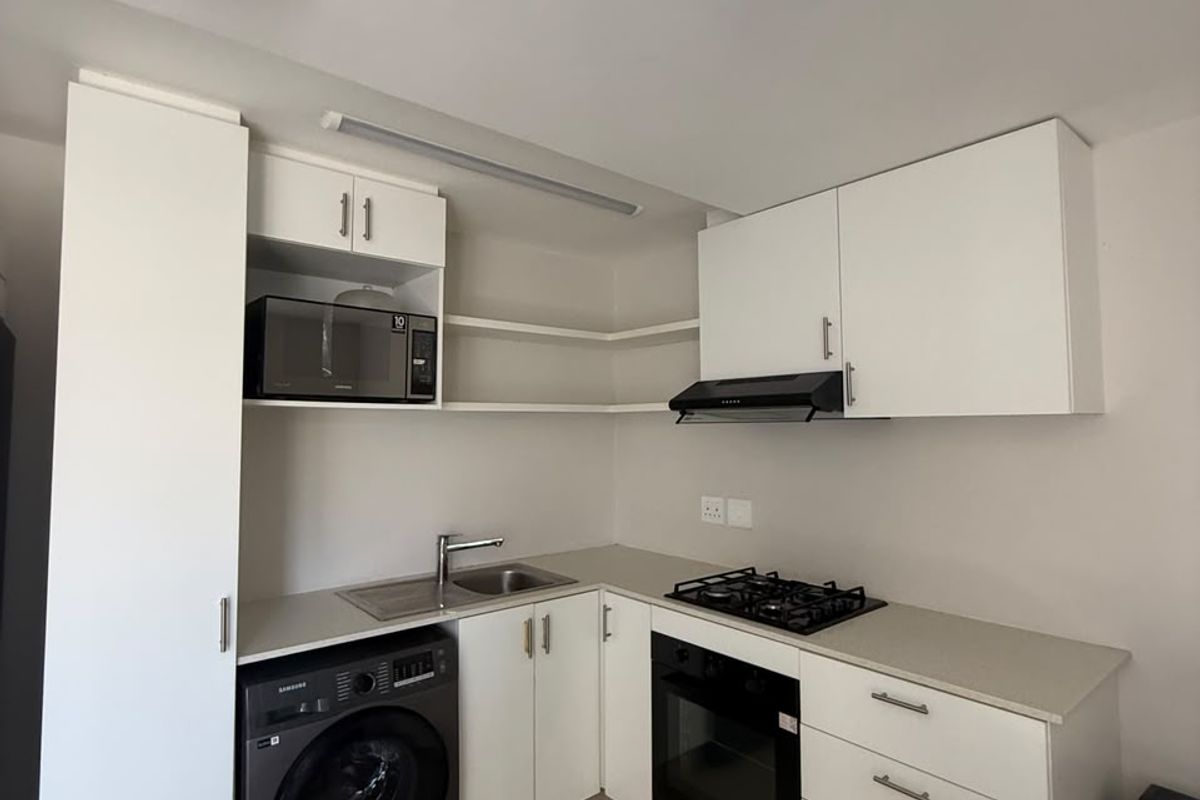 A compact, modern kitchen featuring white cabinetry, a gas hob, built-in oven, extractor fan, and integrated laundry appliance space.