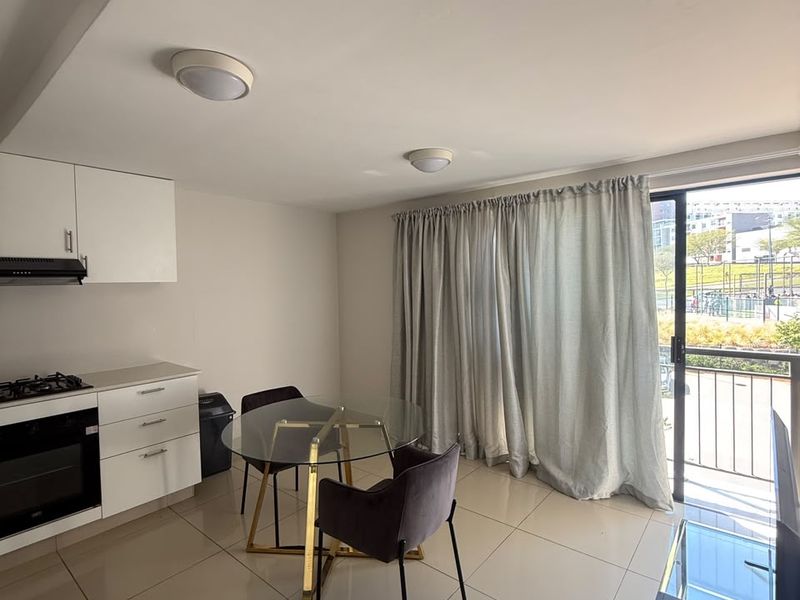 Modern open-plan living area featuring a compact kitchen with built-in appliances, tiled flooring, and direct access to a balcony through sliding glass doors.