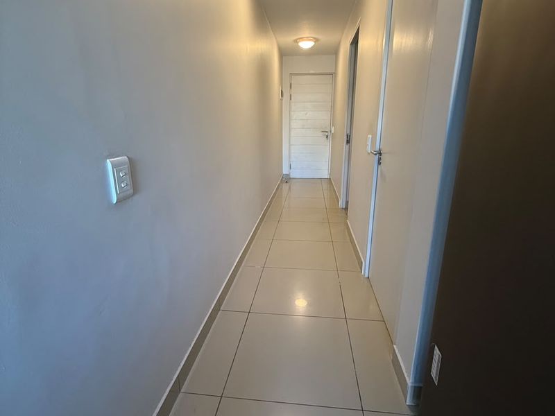 A clean and well-lit hallway featuring neutral tiled flooring and multiple internal doors, providing access to various rooms within the apartment.